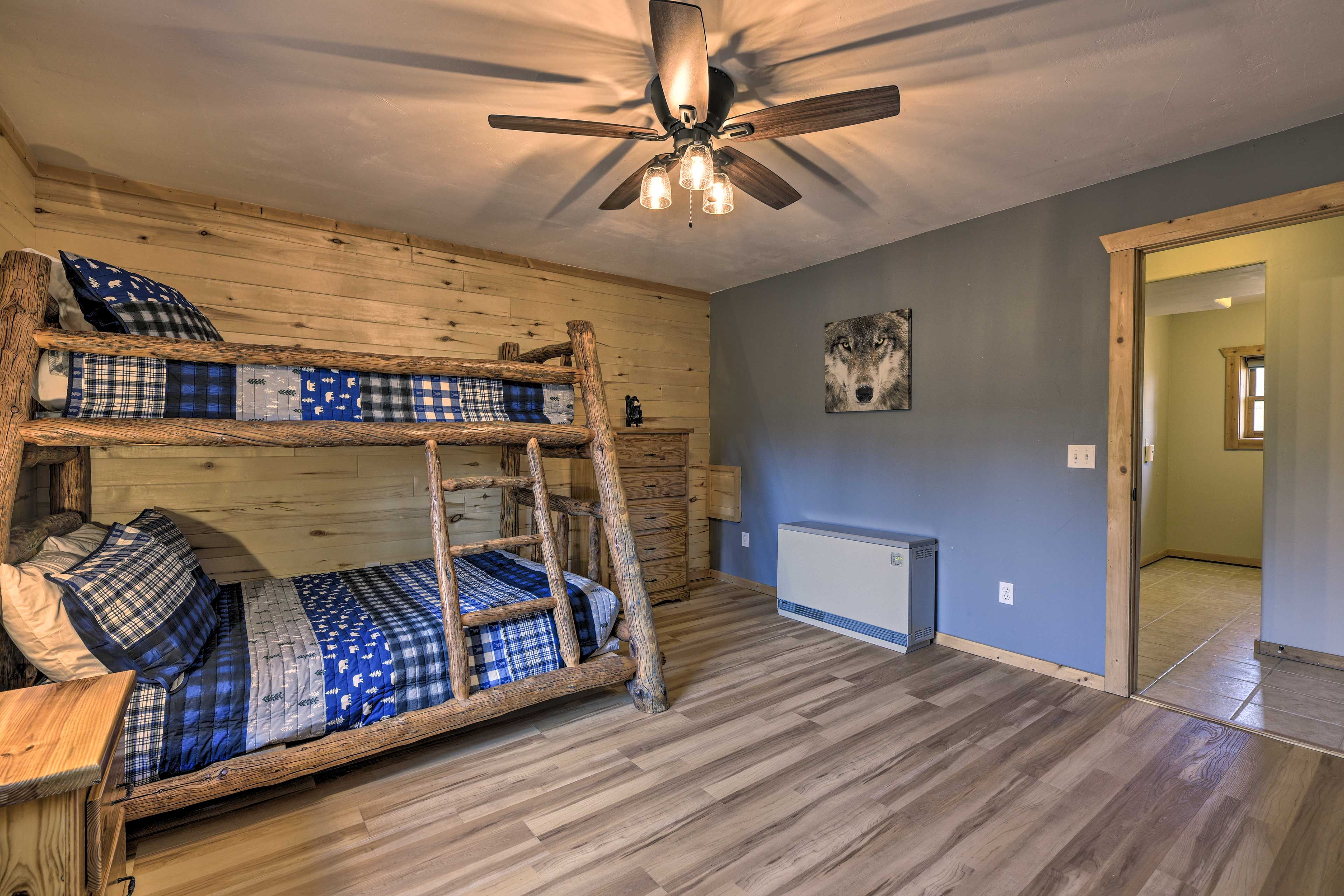 Uma cama beliche com escada de madeira, um ventilador de teto e um radiador em um quarto com piso de madeira e parede azul.
