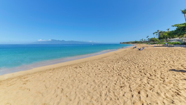 A wide sandy beach with clear blue water and distant mountains. - Island Oasis Near Kaanapali Beach & Black Rock (Kaanapali)