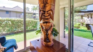 A wooden tiki head sculpture on a table in a room with large windows overlooking a garden and a building. - Island Oasis Near Kaanapali Beach & Black Rock (Kaanapali)