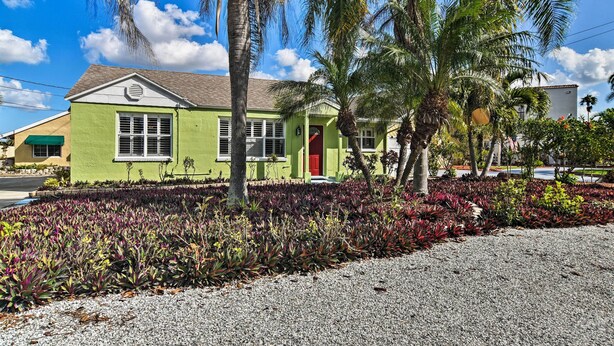 A green building with a red door, surrounded by palm trees and a gravel driveway. - Bayside Pad w/ Pool Access & Dock: 1/2 Mi to Beach (Indian Rocks Beach)