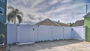 A gated backyard with a concrete patio, a palm tree, and a house in the background. - Bayside Pad w/ Pool Access & Dock: 1/2 Mi to Beach (Indian Rocks Beach)