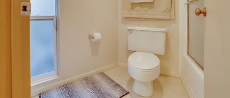 A bathroom with a toilet, a towel rack, a framed picture, and a window.