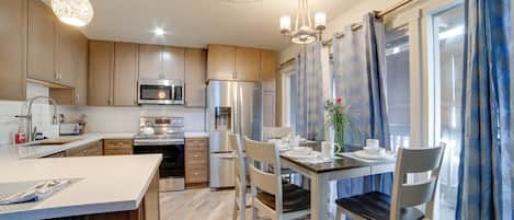A modern kitchen with stainless steel appliances, a dining area with a table set for two, and a large window with blue curtains.