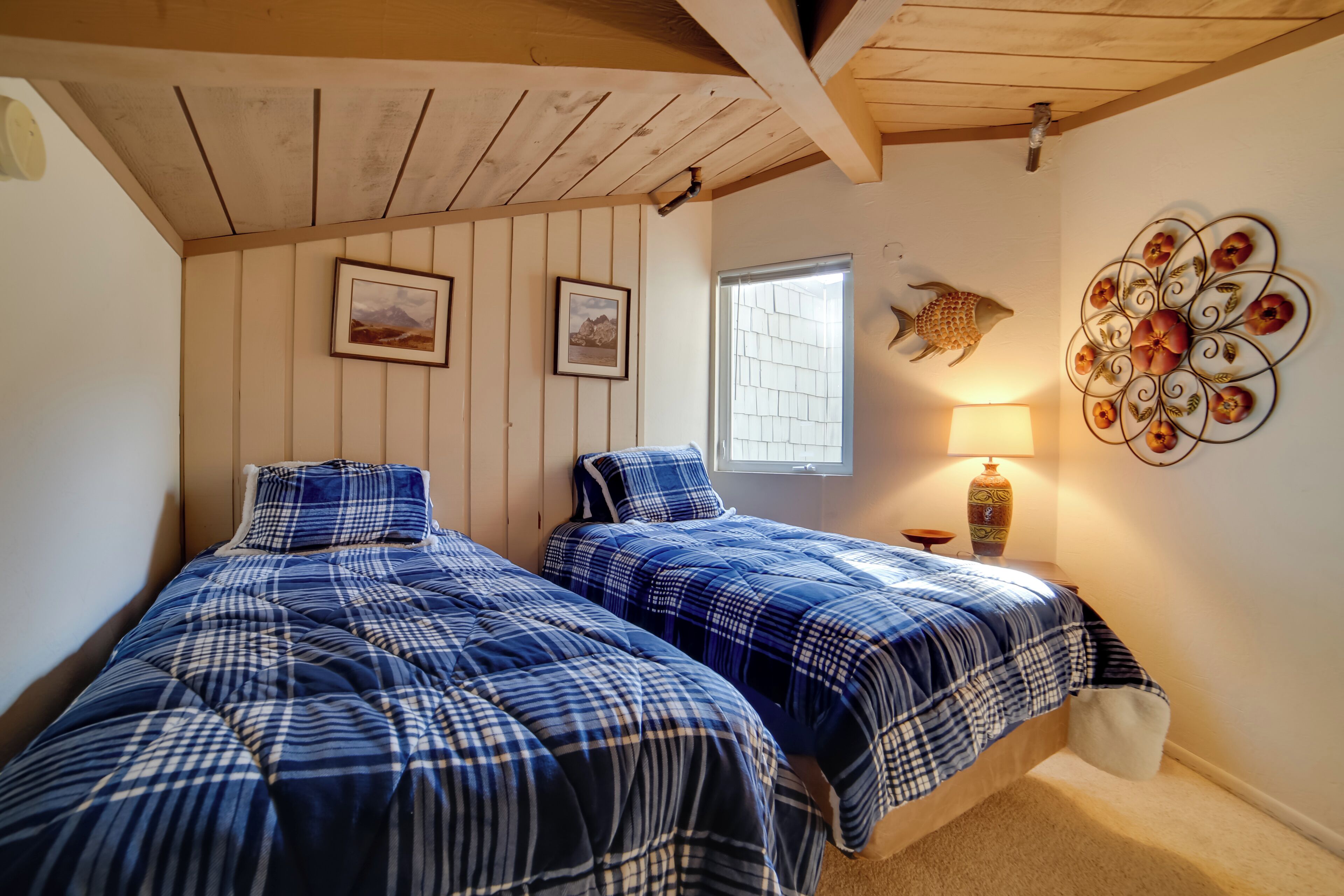 Un dormitorio con dos camas, vigas de madera en el techo, cuadros enmarcados en la pared, una decoración de peces y una lámpara sobre una mesita de noche.