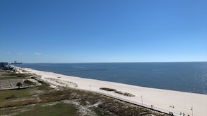 Une scène de plage côtière avec un ciel dégagé, une plage de sable, une jetée qui s’avance dans l’eau et une route menant à la plage.
