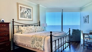 A bedroom with a bed, dresser, and a view of the ocean.