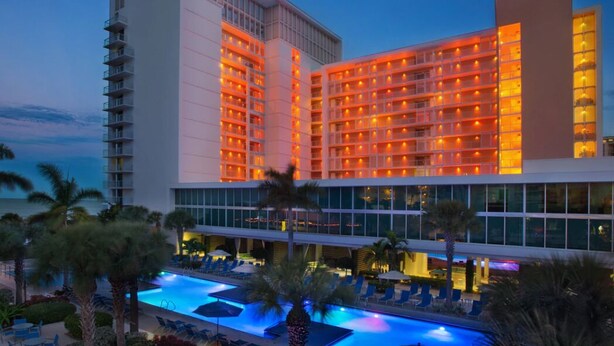 Ein Hotel mit mehreren Etagen, einem Swimmingpool und Palmen.