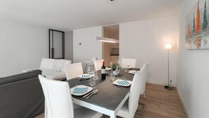 A modern dining area with a table set for four, white chairs, and a sofa in the background. - Lovely apartment in Oostende with WiFi (Oostende)