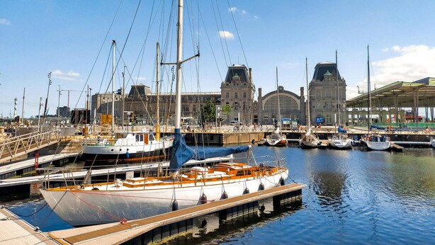 A marina with multiple boats docked, a large building with a distinctive architectural style in the background, and a clear blue sky. - Lovely apartment in Oostende with WiFi (Oostende)