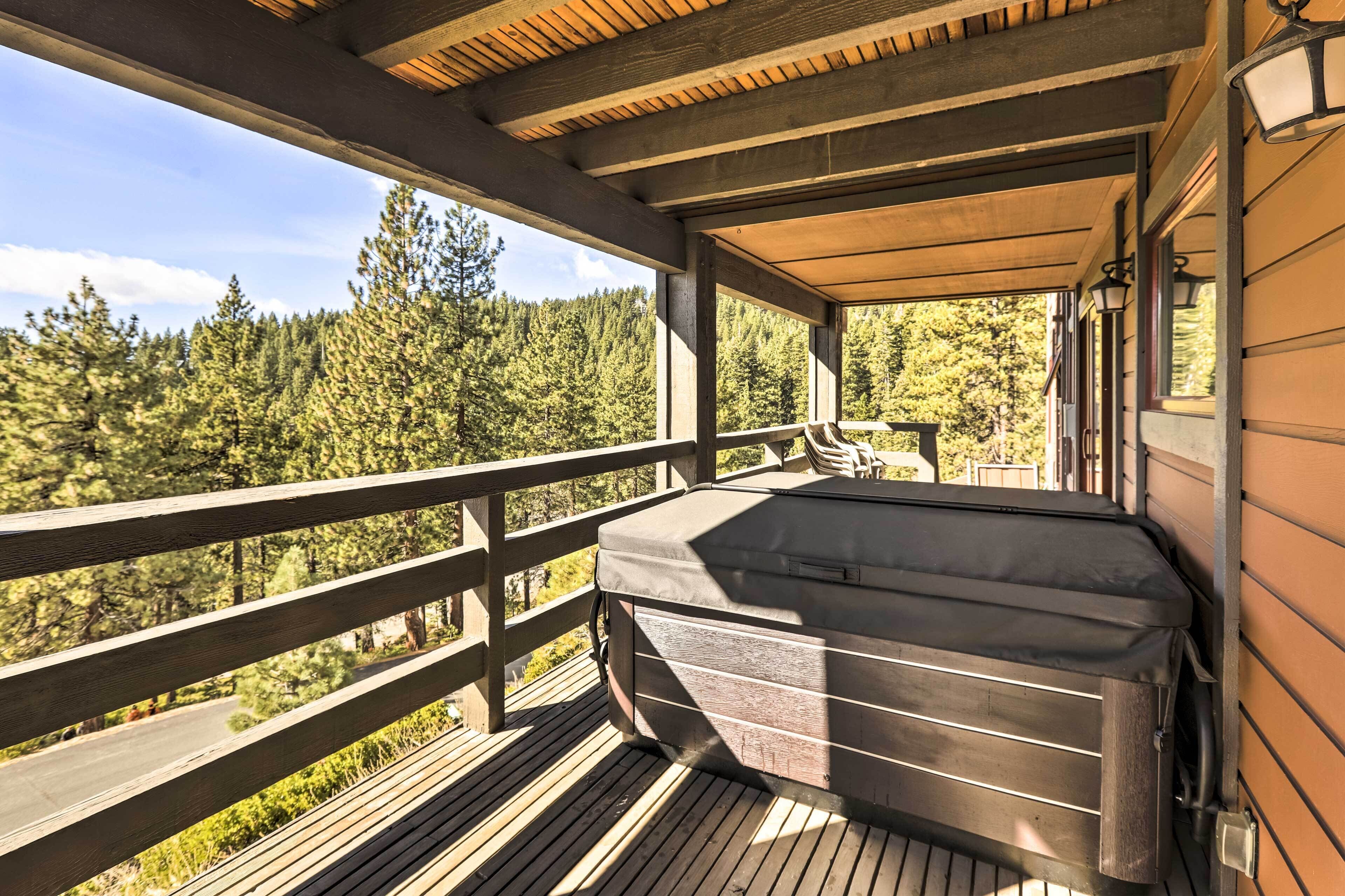A wooden deck with a hot tub, wooden railings, and a view of a forest.