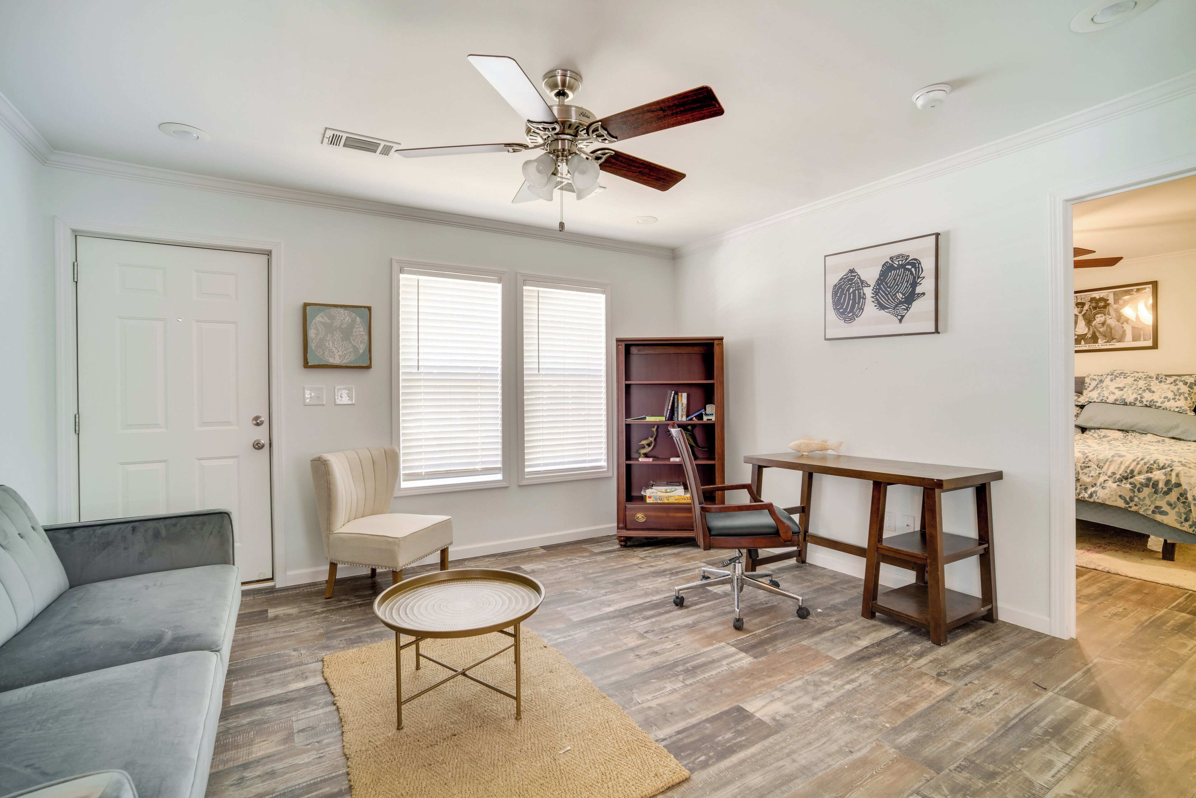 A well-lit room with a ceiling fan, a bookshelf, a desk, a chair, and a sofa.