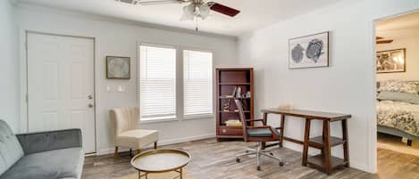 A well-lit room with a ceiling fan, a bookshelf, a desk, a chair, and a sofa.