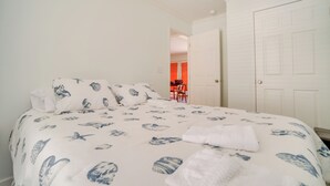A bedroom with a bed, white walls, and a door leading to another room. - Charleston Home w/ Porch - 3 Mi to Folly Beach! (Charleston)