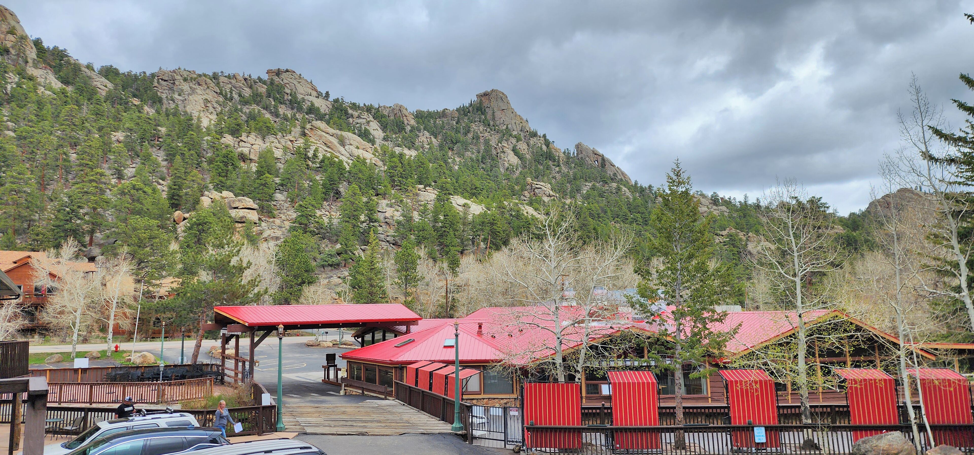 Un albergue de montaña con un edificio de techo rojo, una terraza cubierta y un estacionamiento.