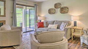 A living room with a sofa, armchairs, a small wooden side table, and a floor lamp. There is a sliding glass door leading to a patio with a view of a lawn. - Pet-friendly Branson Retreat w/ Pool & Golf Access (Branson)