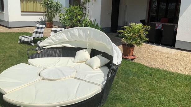 A sunbed with a canopy, surrounded by potted plants, in a well-maintained outdoor area with a building in the background. - Brenda Ferienwohnung (Schillingsfürst)