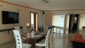 A spacious living area with a dining table, white chairs, a flat-screen TV, and a sofa. - Brenda Ferienwohnung (Schillingsfürst)