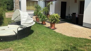 A covered outdoor seating area with a grill, potted plants, and a stone pillar. - Brenda Ferienwohnung (Schillingsfürst)