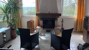 A living room with a stone fireplace, two wicker chairs, a coffee table, and a potted plant. - Brenda Ferienwohnung (Schillingsfürst)