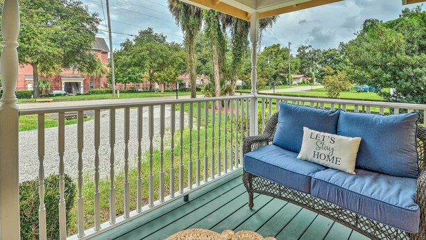 A covered porch with a wicker sofa and a cushion that says "Let's Stay Home." - Family Home: Walk to Downtown & Stetson Univ! (DeLand)