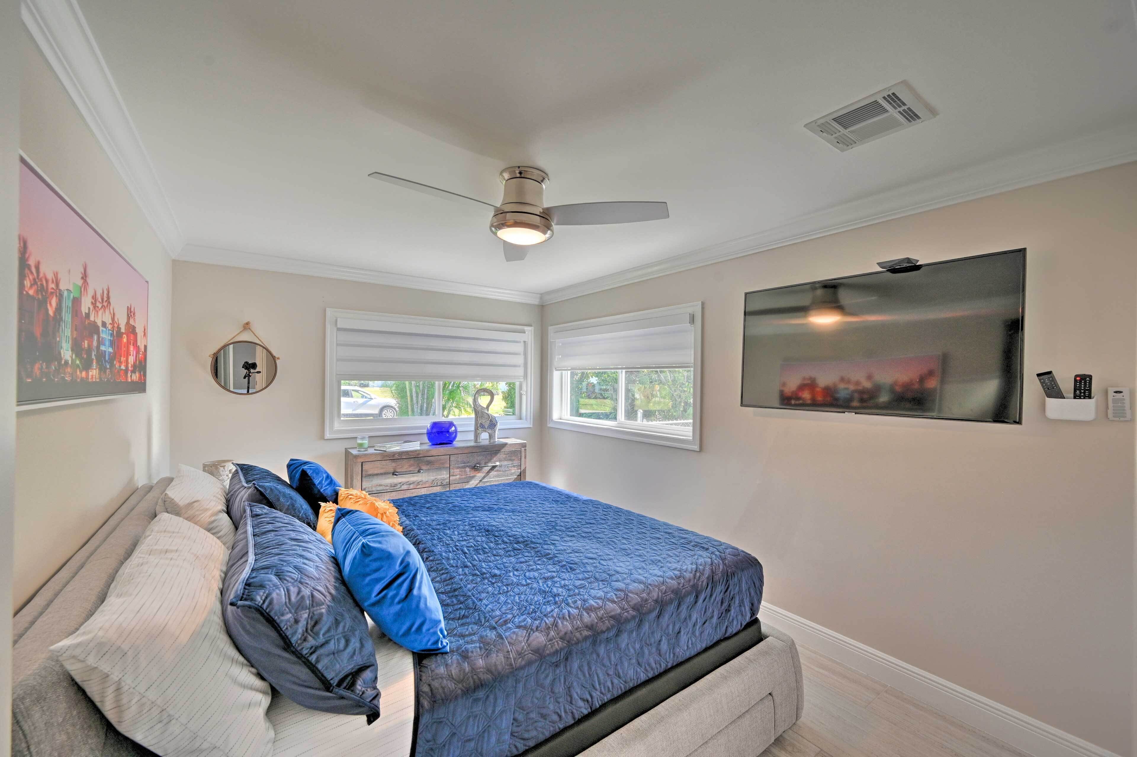 A bedroom with a bed, a ceiling fan, a TV, and a window with blinds.
