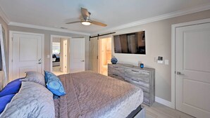 Un dormitorio con cama, cómoda, ventilador de techo y televisor en la pared.