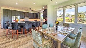 A modern kitchen with dark cabinets, a central island, and a dining area with a wooden table set for four. - Spacious Kauai Getaway < 1 Mi to the Ocean! (Princeville)