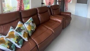 Un salón espacioso con un sofá de cuero marrón, cojines estampados y cortinas rojas.