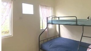 Una habitación pequeña y sencilla con una cama nido, dos ventanas con cortinas y una pared blanca lisa.