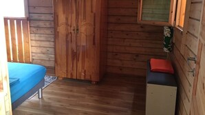A wooden cabin room with a bed, wardrobe, and a small table. - Charming, air-conditioned chalet in the heart of Saint-Leu, 5 minutes from the beach (Saint-Leu)