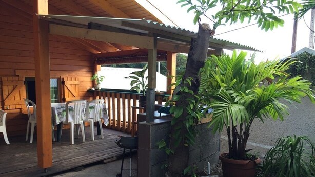A covered outdoor seating area with tables and chairs, a wooden deck, and potted plants. - Charming, air-conditioned chalet in the heart of Saint-Leu, 5 minutes from the beach (Saint-Leu)