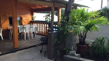 A covered outdoor seating area with tables and chairs, a wooden deck, and potted plants.