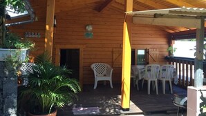 A wooden cabin with a covered porch, white plastic chairs, and a potted plant. - Charming, air-conditioned chalet in the heart of Saint-Leu, 5 minutes from the beach (Saint-Leu)