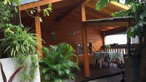A wooden cabin with a covered porch, potted plants, and outdoor seating. - Charming, air-conditioned chalet in the heart of Saint-Leu, 5 minutes from the beach (Saint-Leu)