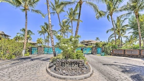 A paved area with a sign reading "Hali Kai" surrounded by palm trees and a stone wall.