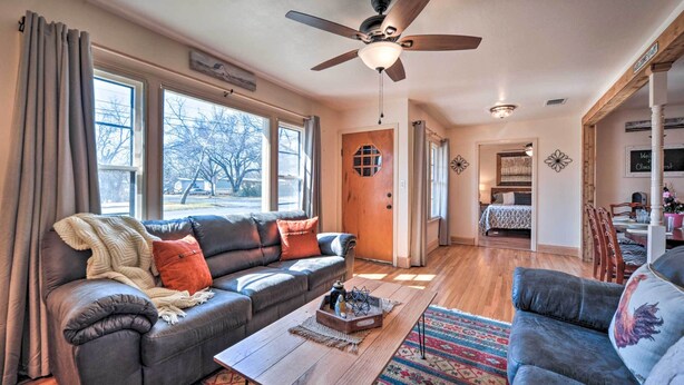 A spacious living room with a dark leather sofa, a wooden coffee table, and a blue armchair. A ceiling fan and a wooden door are visible in the background. - 1 Mi to Dtwn Fredericksburg: Quiet Getaway w/ Yard (Fredericksburg)