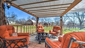 A covered patio with orange upholstered chairs and a star-patterned table, overlooking a fenced yard with trees and buildings. - 1 Mi to Dtwn Fredericksburg: Quiet Getaway w/ Yard (Fredericksburg)