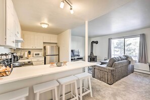 Et moderne køkken med hvide skabe, en stor ø med barstole, et indbygget komfur og et hyggeligt opholdsområde med en sofa og pejs.