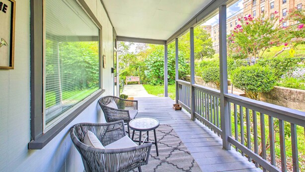 Eine überdachte Veranda mit Korbstühlen und einem kleinen Tisch, mit Blick auf einen Garten und ein Backsteinhaus.