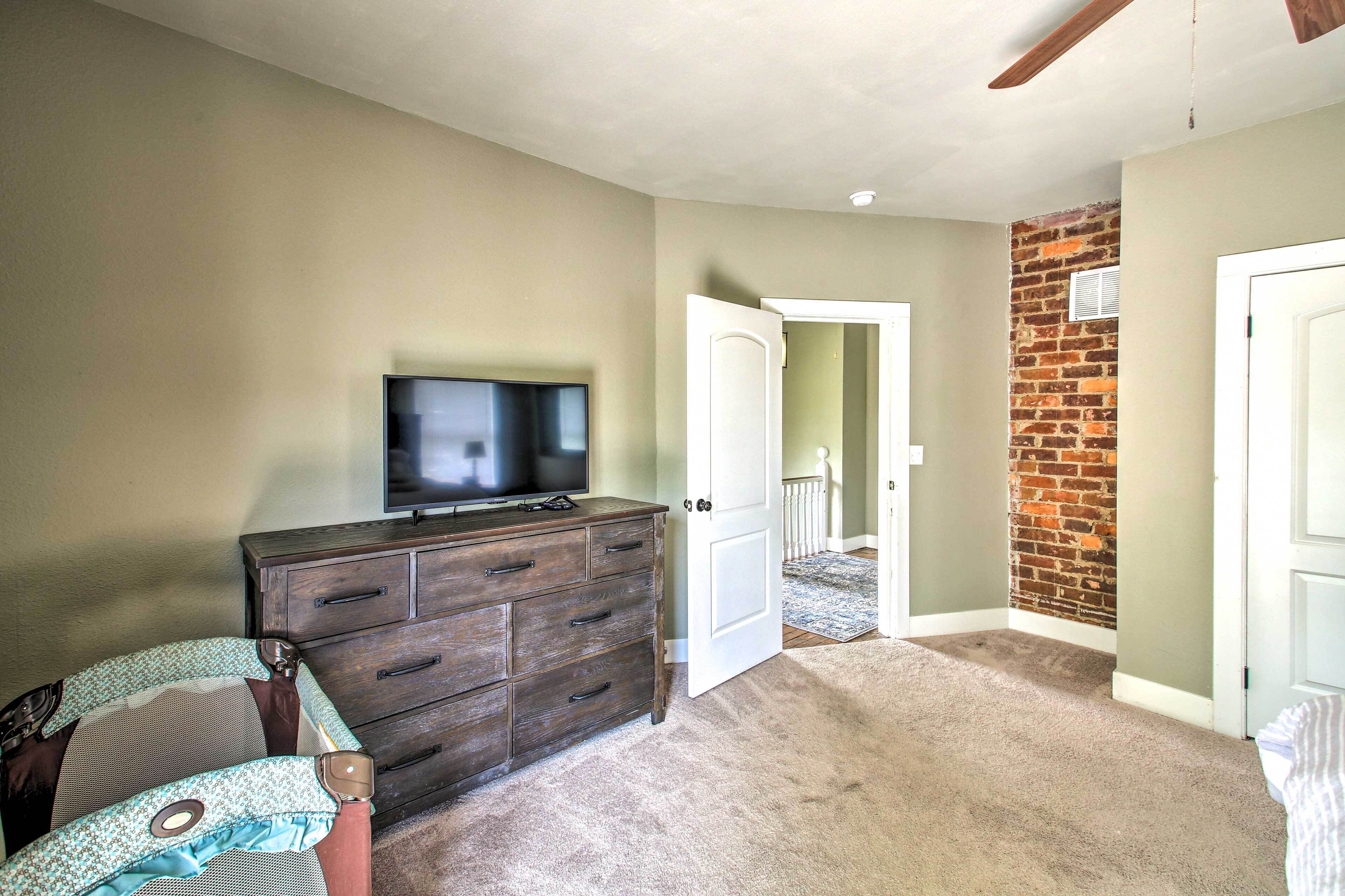 A bedroom with a TV on a dresser, a door leading to another room, and a brick wall.