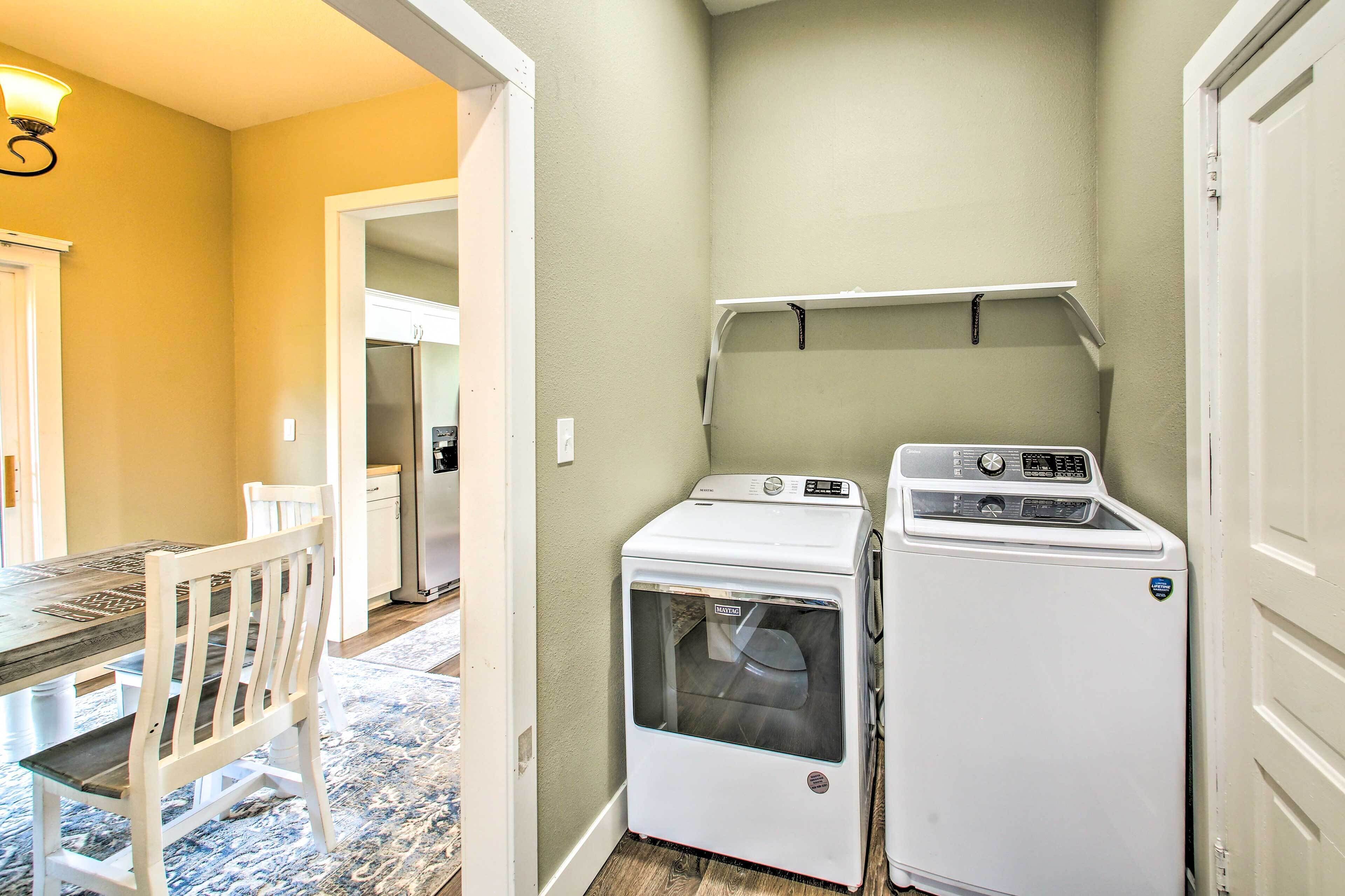 A laundry room with two white appliances, a table with chairs, and a door leading to another room.