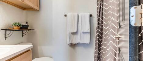A bathroom with a toilet, a sink, a wooden cabinet, a towel rack with two towels, and a shower curtain with a pattern.