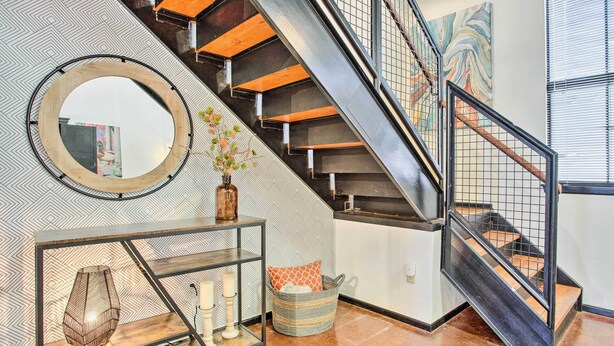 A staircase with wooden steps and metal railings, a round mirror on the wall, a console table with decorative items, and a patterned wall. - Norman, Oklahoma, Vacation Rental 1 Mi to OU! (Norman)