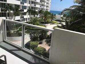 A balcony with a view of a landscaped courtyard, palm trees, and a building with a white facade.