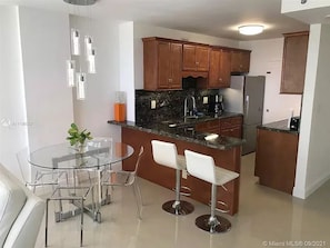 A modern kitchen with wooden cabinets, a stainless steel refrigerator, and a glass dining table with bar stools.