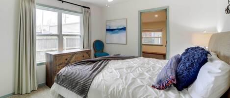 A bedroom with a bed, a ceiling fan, a window with curtains, a chair, and a painting on the wall.
