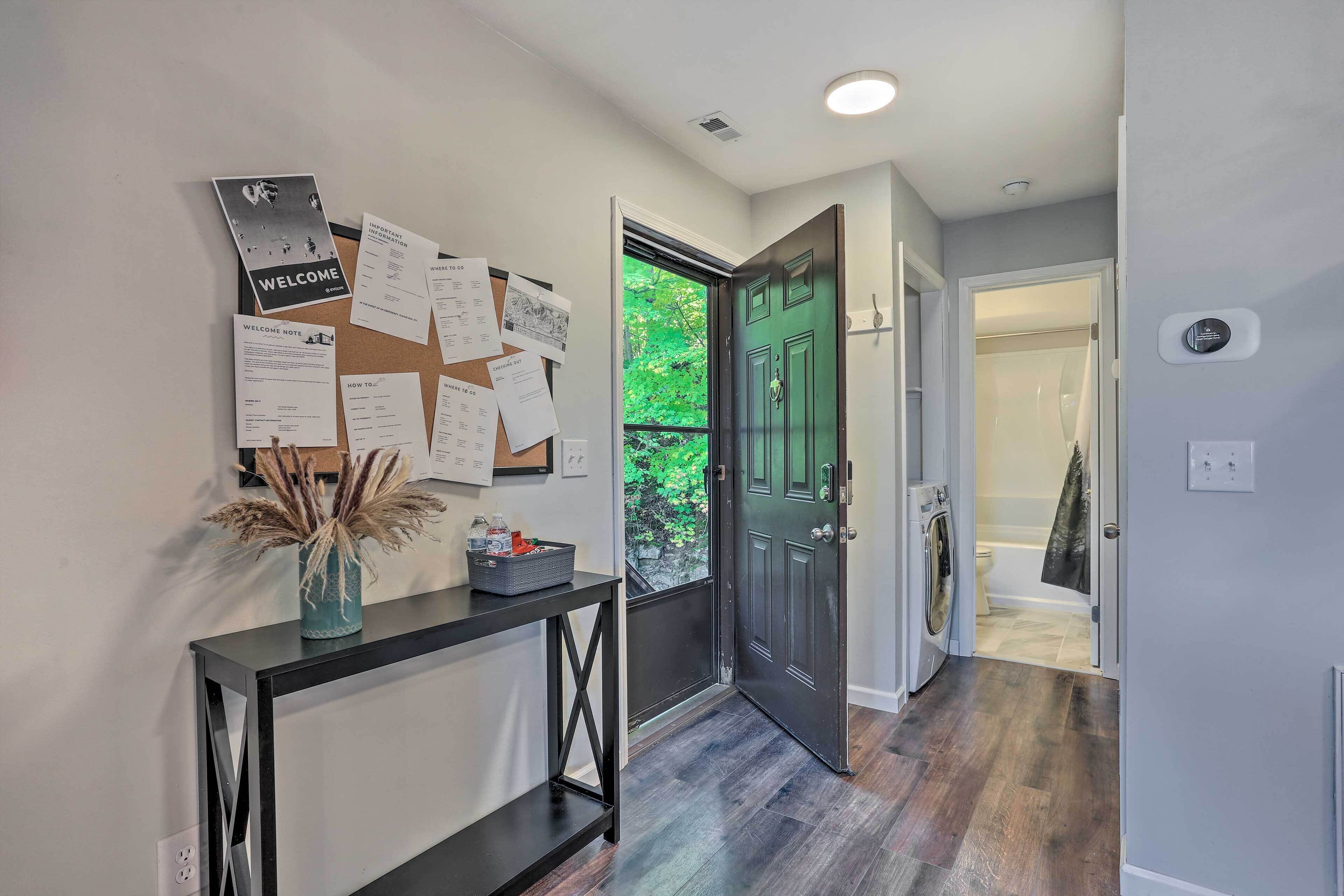 A hallway with a bulletin board, a welcome sign, and a door leading to a bathroom.