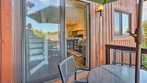 Una terraza de madera con puerta de vidrio que da a una zona de cocina, una mesa con sillas y un paraguas verde.