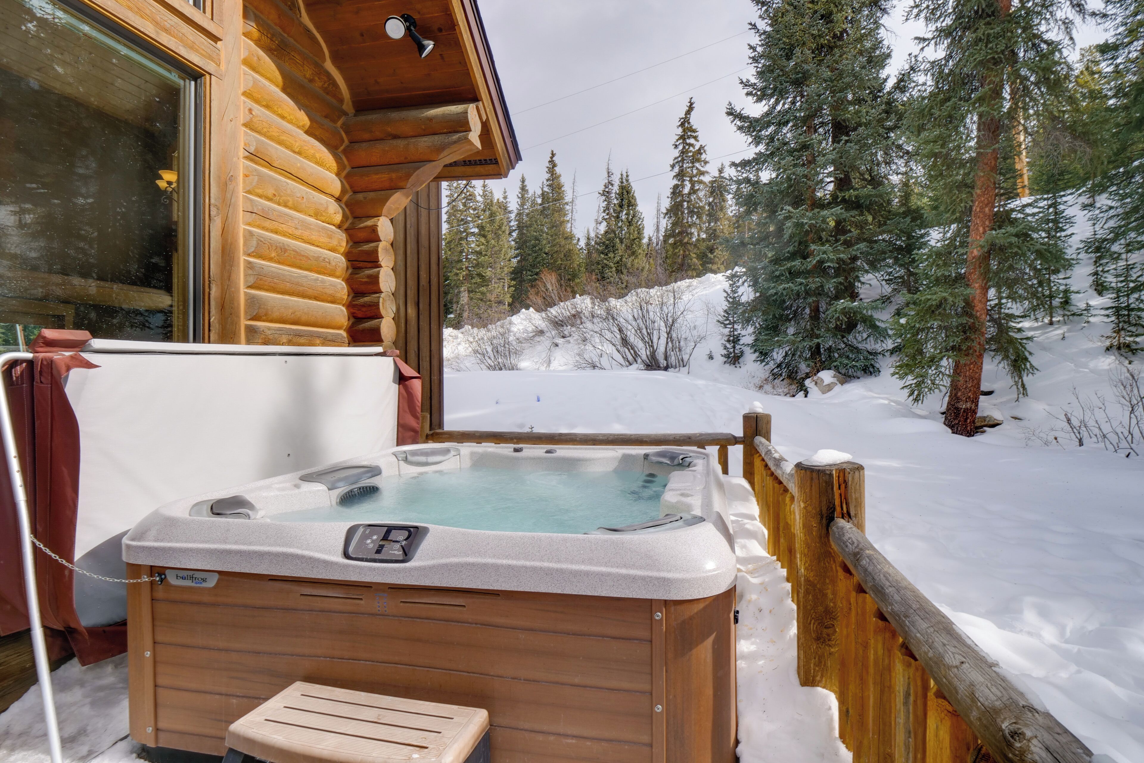 A wooden cabin with a hot tub in the snow.