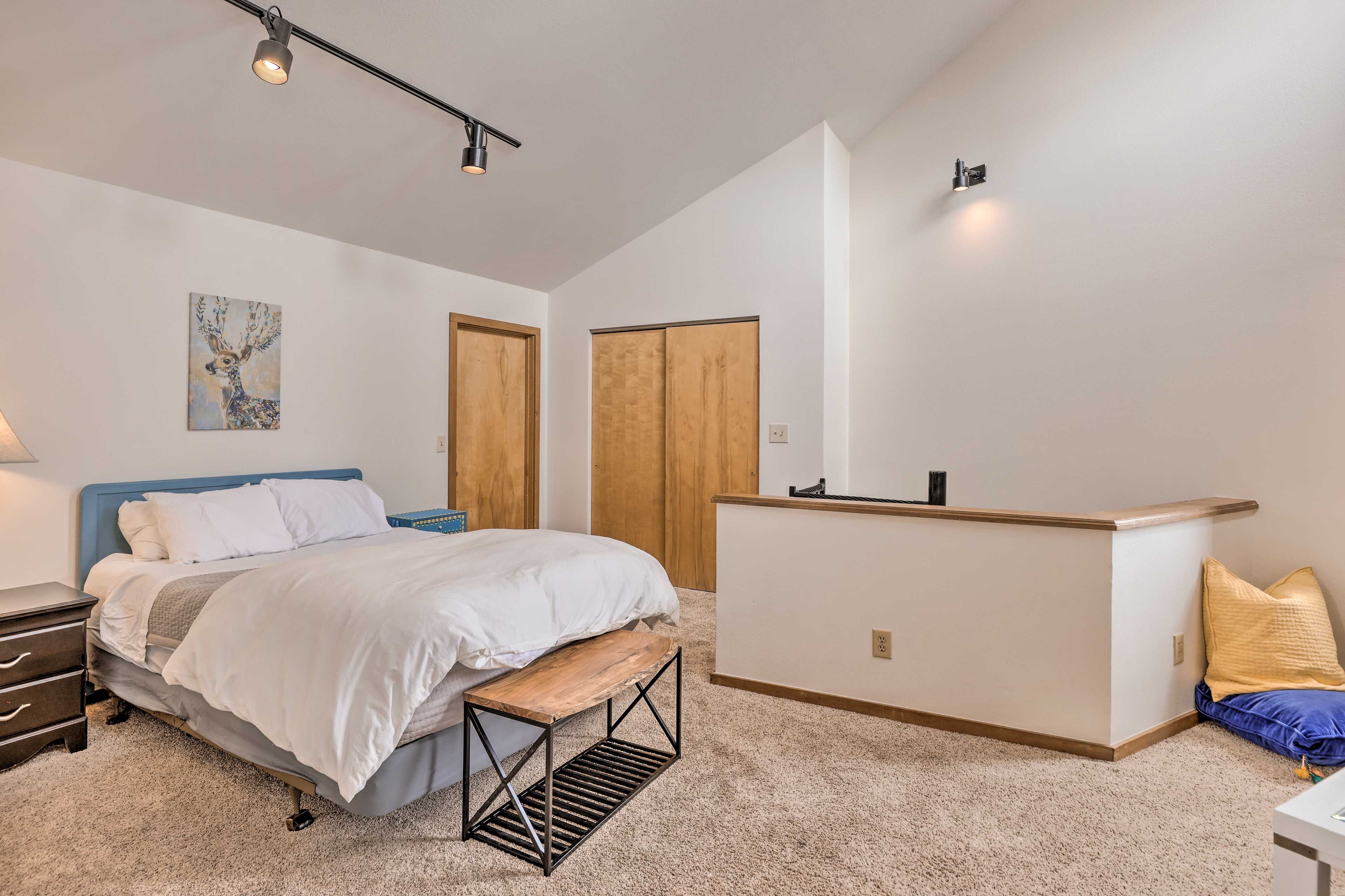A bedroom with a bed, bedside table, bench, and a small desk area.